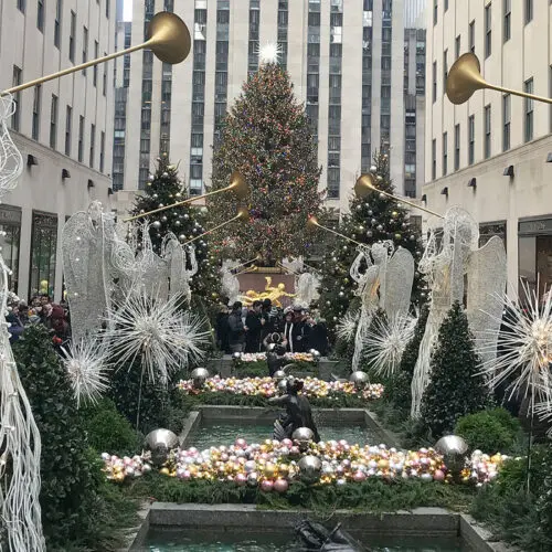 Holiday decorations and large christmas tree at rockefeller center, surrounded by angel statues and festive lights.