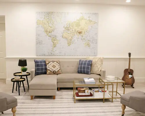 A stylish living room featuring a large world map on the wall, a sectional sofa with cushions, two armchairs, a coffee table, and a guitar in the corner.