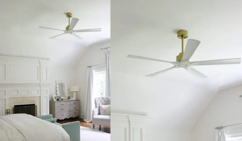 A bedroom with white walls and ceiling features a white ceiling fan with gold accents, a fireplace, a dresser with a mirror, a bed, and a cushioned chair by the window with light curtains.