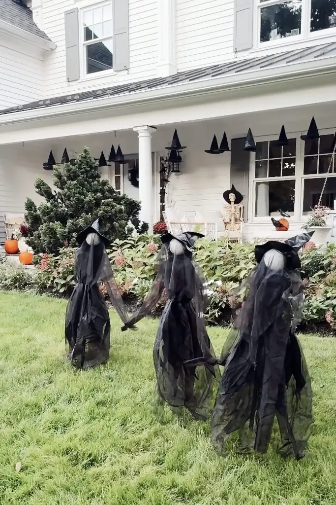 Transform Your Home into a Witch’s Haven! Three witch decorations in black veils stand on a lawn in front of a house adorned with pumpkins and witch hat decorations.