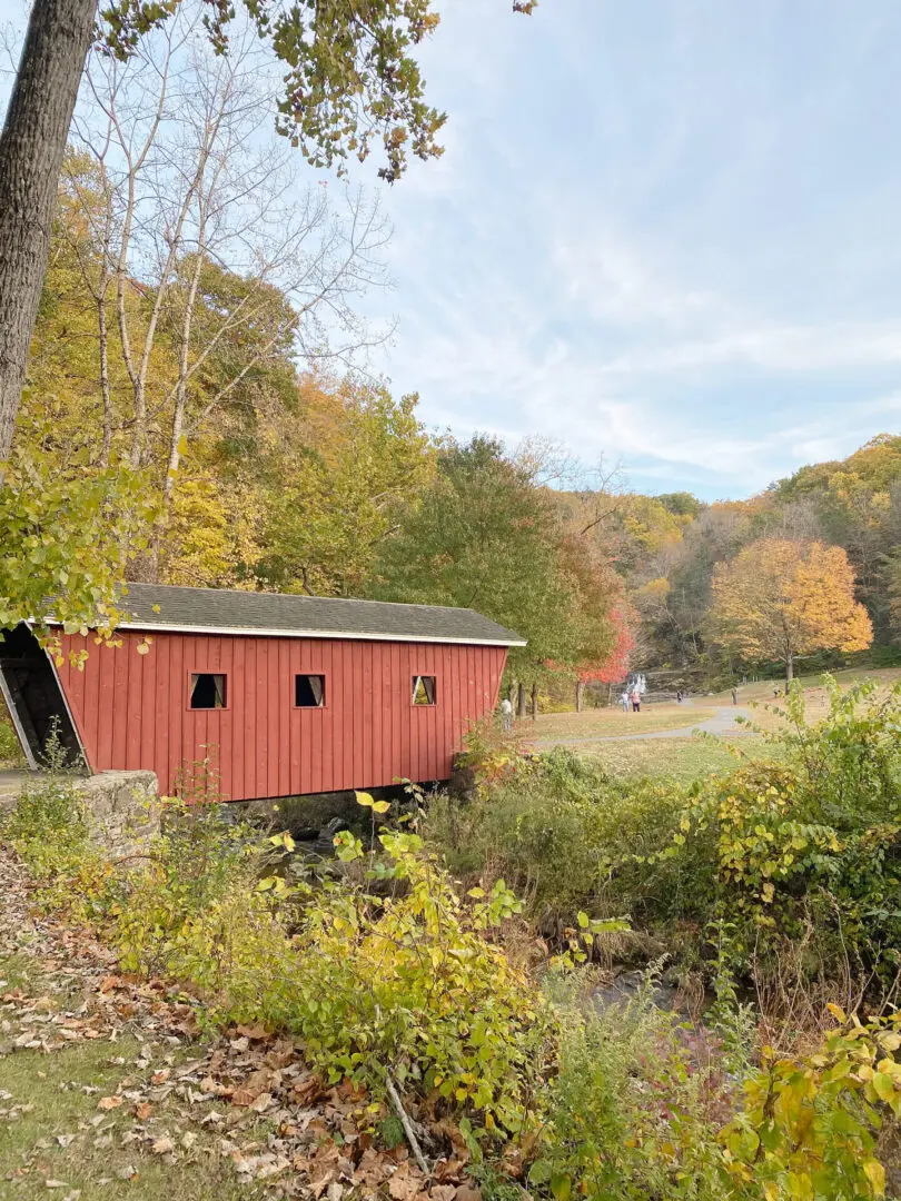 Your Guide to the Best Fall Activities Near Fairfield County, Connecticut in the month of October from pumpkin patches to haunted houses! A red covered bridge spans a small creek surrounded by autumn trees and foliage.