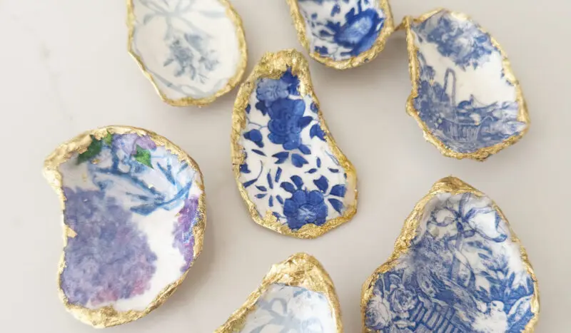 Seven oyster shells with blue and white floral patterns and gold edges are arranged on a white surface.