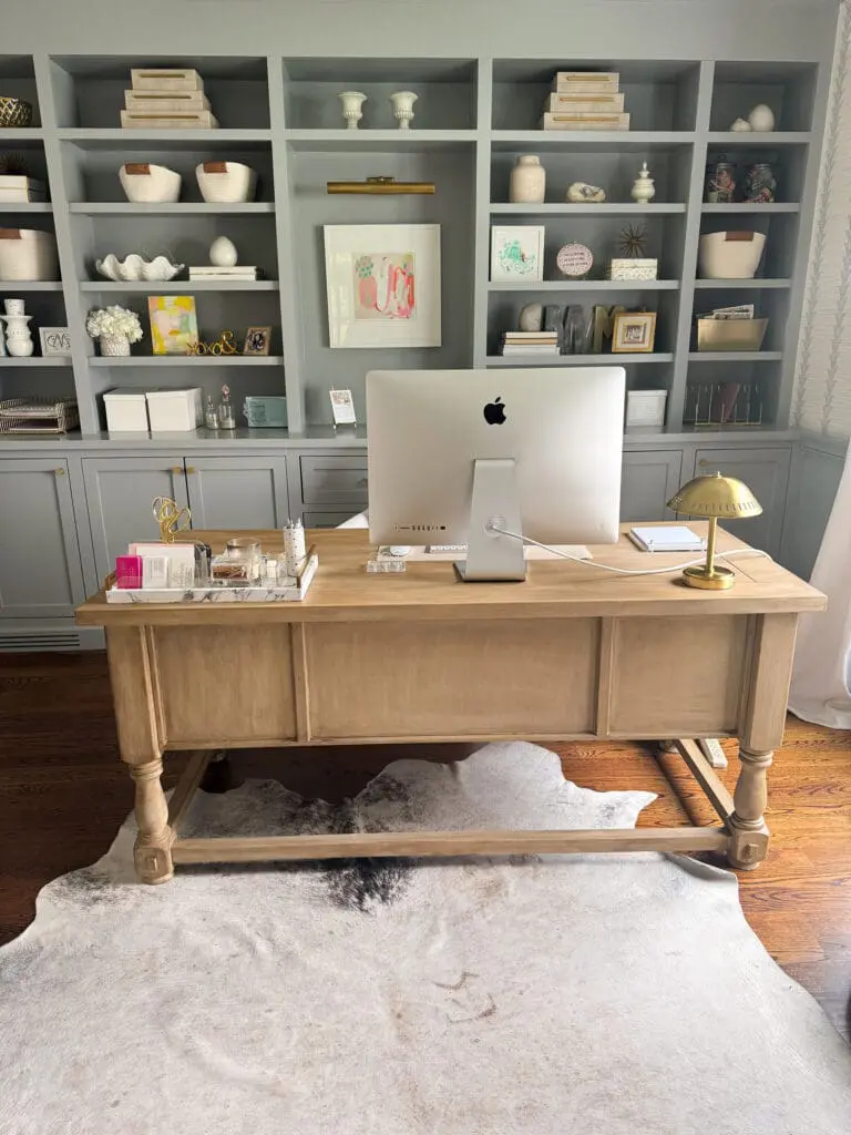 DIY Pottery Barn Finish Furniture || Darling Darleen Top Lifestyle Blogger A home office setup with a wooden desk, iMac computer, desk lamp, and organized shelves filled with books, decor, and artwork against a gray built-in shelving unit.