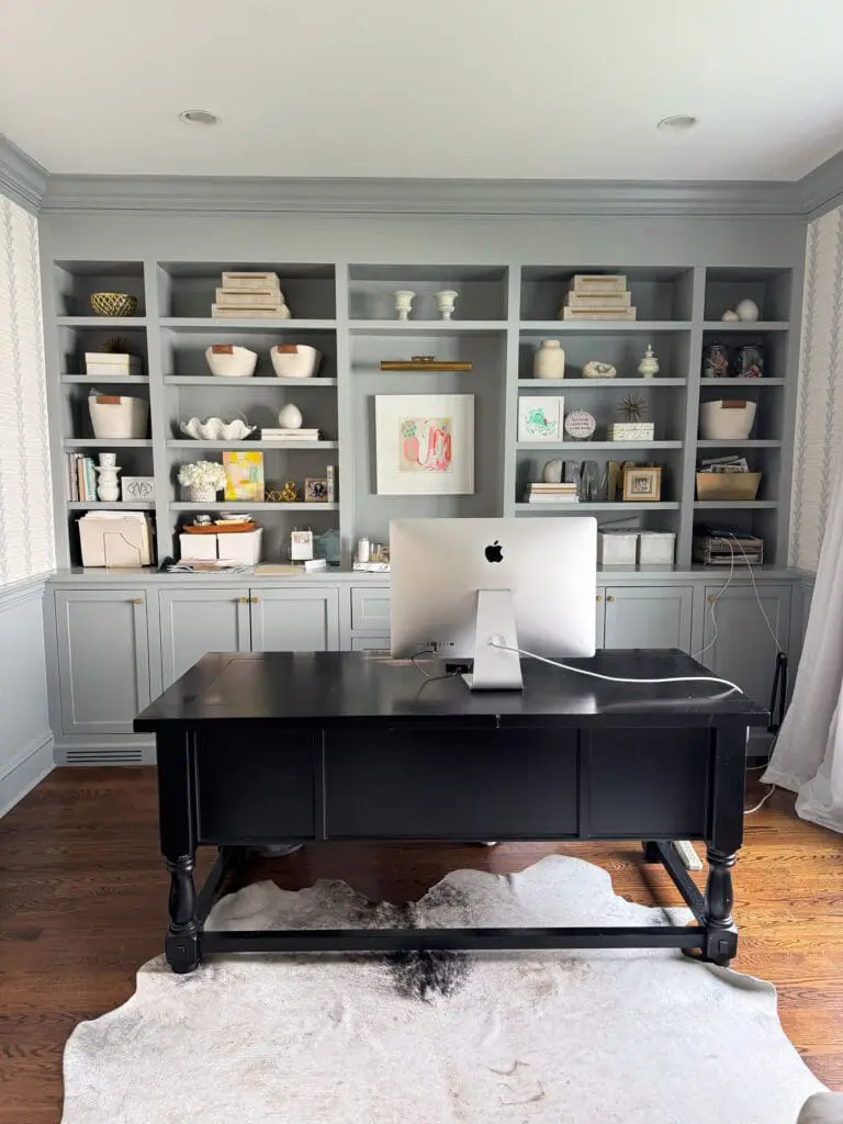DIY Pottery Barn Finish Furniture || Darling Darleen Top Lifestyle Blogger A home office with a black desk, an iMac, built-in gray bookshelves filled with decor, books, and art, and a cowhide rug on a wooden floor.