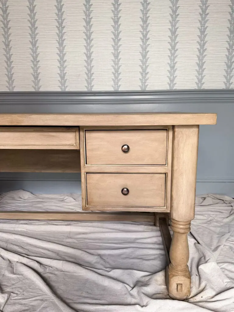DIY Pottery Barn Finish Furniture || Darling Darleen Top Lifestyle Blogger  A wooden desk with two drawers stands on a drop cloth in front of patterned wallpaper and a blue wainscoting wall.
