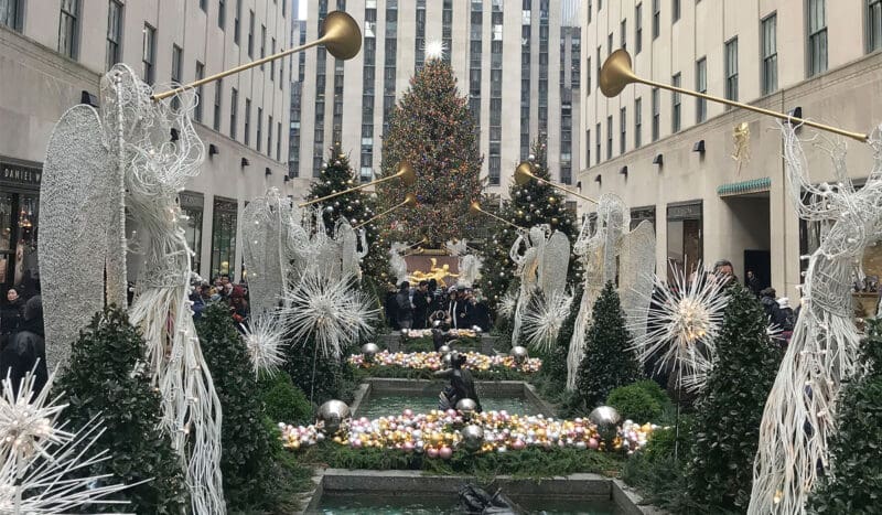 Holiday decorations and large christmas tree at rockefeller center, surrounded by angel statues and festive lights.