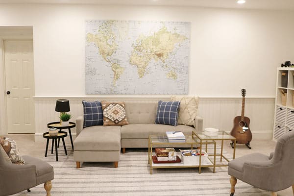 A stylish living room featuring a large world map on the wall, a sectional sofa with cushions, two armchairs, a coffee table, and a guitar in the corner.