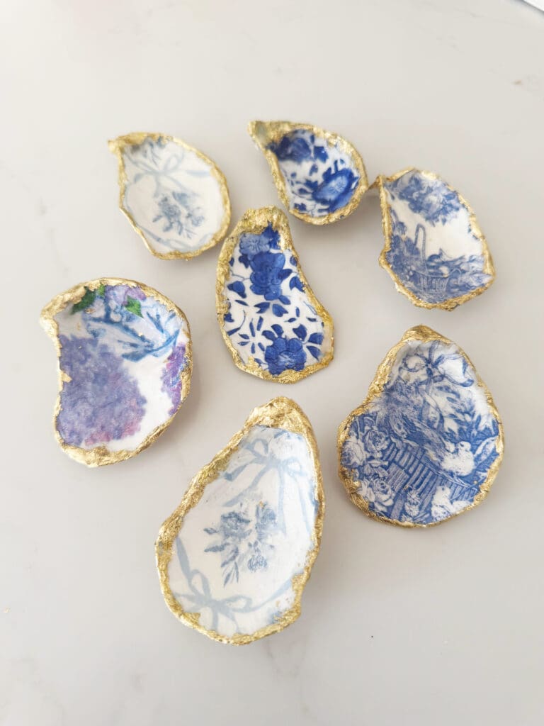 Seven decorative oyster shells with blue and white floral patterns and gold edges are arranged on a white surface.
Easy DIY oyster shell ring dish using paper napkins that is a beautiful gift to give for Easter or Mother's day or make for yourself. 
