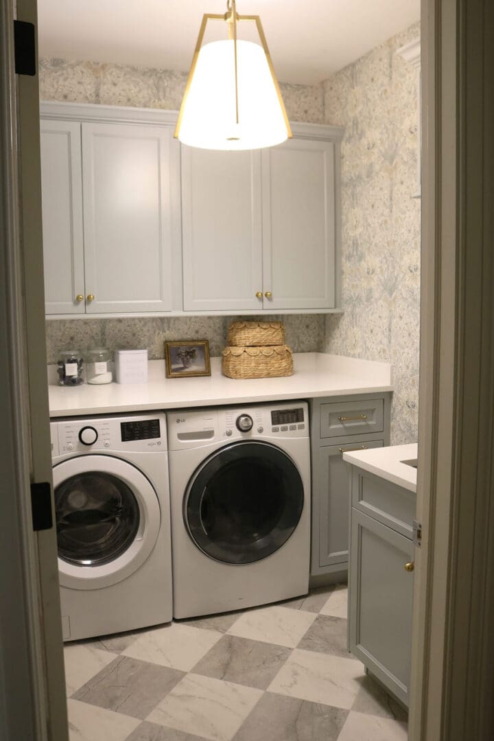 Laundry Room Renovation: Before and After 
Darling Darleen || Top CT Lifestyle Blogger A laundry room with a front-loading washer and dryer, gray cabinets, marble tile floor, overhead light, woven baskets, and a small framed photo on the counter.