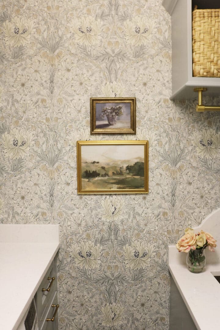 Laundry Room Renovation: Before and After 
Darling Darleen || Top CT Lifestyle Blogger
A small section of a room with patterned wallpaper, two framed landscape paintings on the wall, and a white countertop with a vase of flowers.