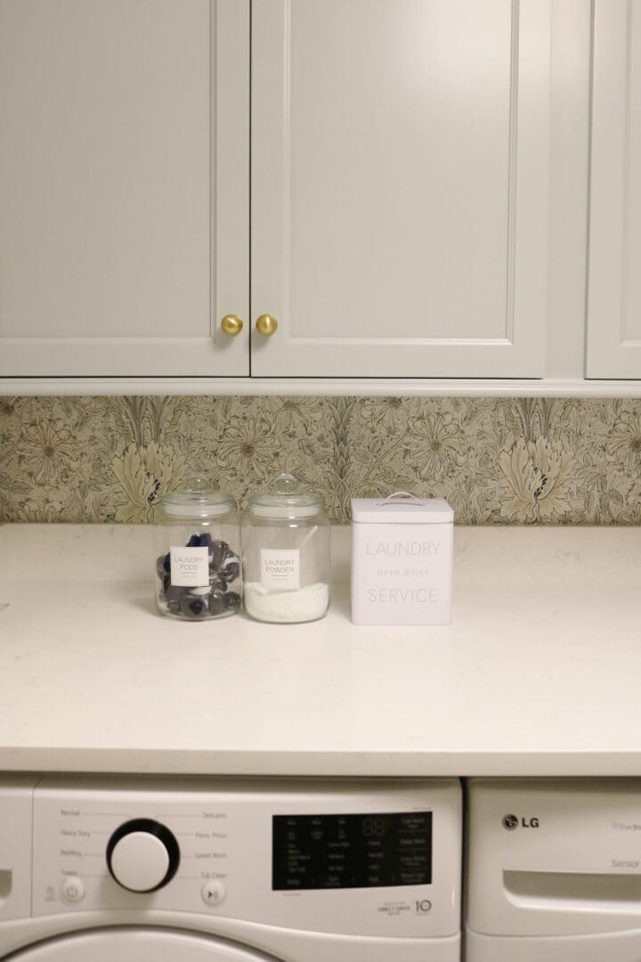 Laundry Room Renovation: Before and After 
Darling Darleen || Top CT Lifestyle Blogger
White laundry room with a countertop holding two labeled jars—one with laundry pods and one with powder—and a box labeled "Laundry Service." Washer and dryer beneath counter.